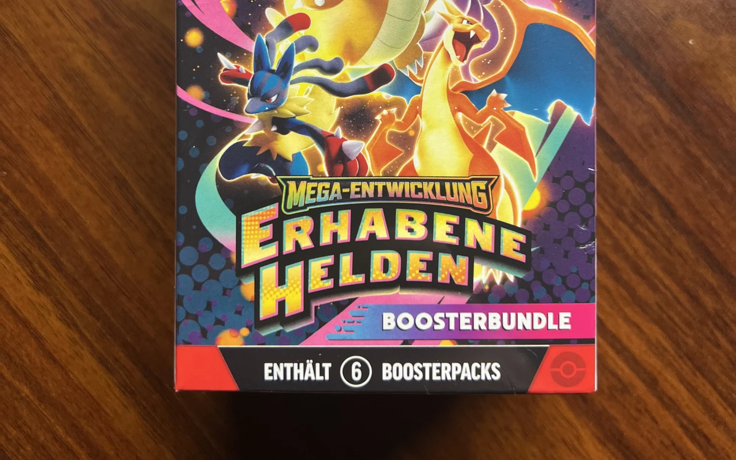 Ein Pokémon-Boosterbundle der Erweiterung Mega-Entwicklung Erhabene Helden auf einem Holztisch, unten der Hinweis auf sechs Boosterpacks.