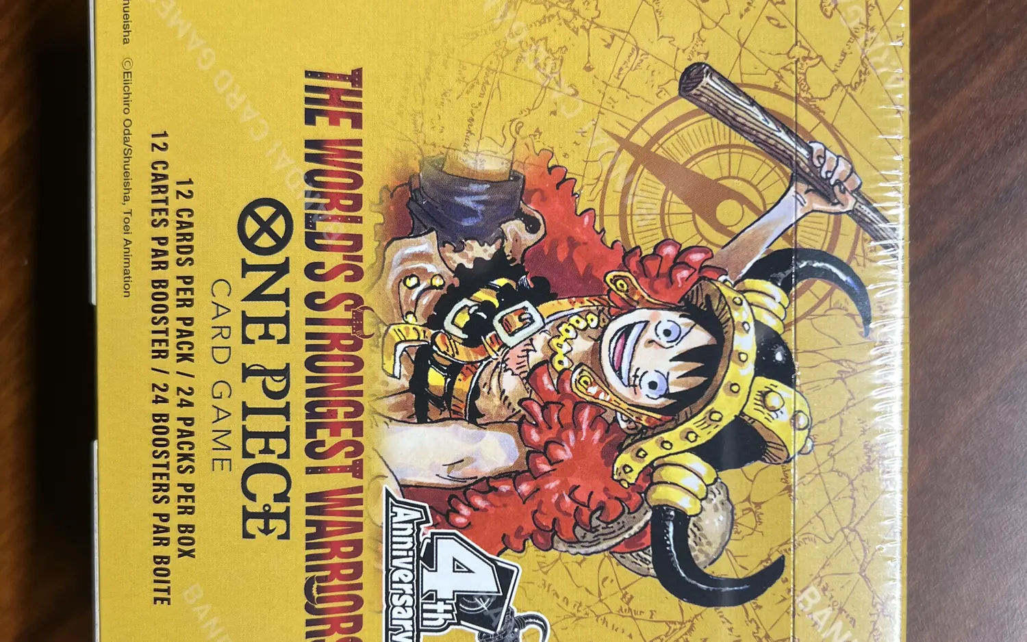 Versiegeltes Display des One Piece Card Game The World's Strongest Warriors OP-17 auf einem Holztisch, mit dem Aufdruck 12 cards per pack und 24 packs per box