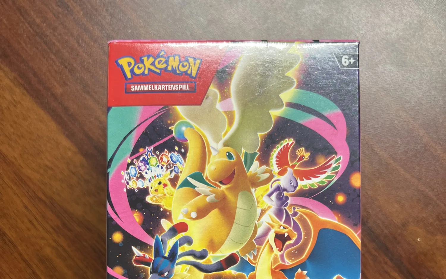 Eine eingeschweißte Pokémon-Packung, auf der Schachtel Dragoran, Ho-Oh, Mewtu, Lucario und Glurak vor buntem Hintergrund.