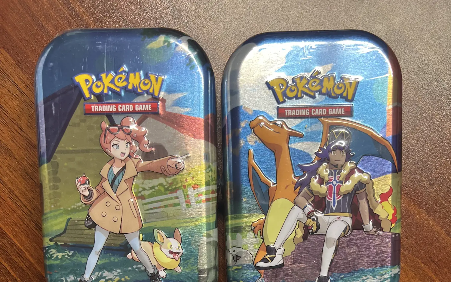 Zwei Pokémon-Mini-Tins nebeneinander auf einem Holztisch, jede mit einer eigenen Illustration aus dem Sammelkartenspiel.